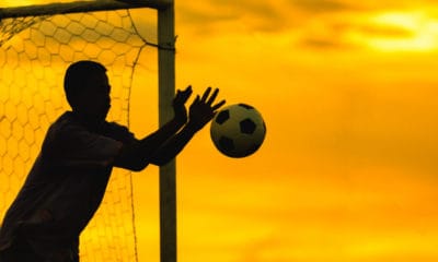 Soccer goalkeeper blocking shot in net yellow sunset background